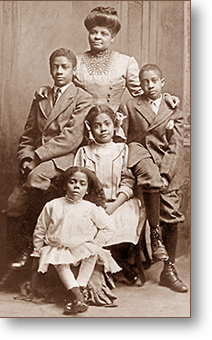 Studiofoto av Ida och hennes fyra barn. Hon står längst bak, pojkarna sitter på karmarna till en stol som äldsta dottern sitter på och minstingen sitter på en pall nedanför. Flickorna har vita klänningar, pojkarna kostym.