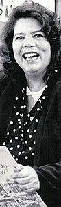 Avlångt foto av skrattande Wilma Mankiller. På fotot som poppar upp då du klickar på denna bild är hon omgiven av barn i en skola och hon håller i en skolbok