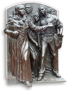 Foto av bronsstaty mot en vägg utomhus, av Harriet Tubman som leder ett antal flyende slavar