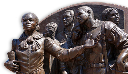 Foto av del av bronsstaty mot en vägg utomhus, av Harriet Tubman som leder ett antal flyende slavar