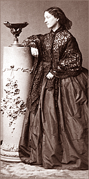 Foto av Jeanne stående bredvid en pelarliknande piedestal med en skål på. Hon står i profil och lutar ena armen mot piedestalen
