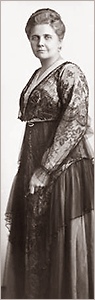 Foto av Ninni Kronberg iförd en tjusig klänning. Hon står vänd åt sidan men vrider huvudet och ser in i kameran