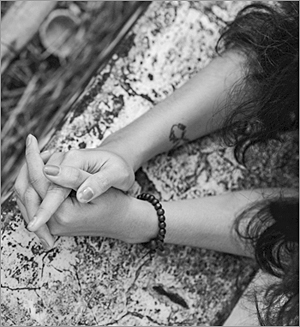 Foto av en kvinnas underarmar och händer, som vilar mot en stenmur. Hon har ett armband av pärlor och lite mörkt, lockigt hår syns i utkanten av bilden