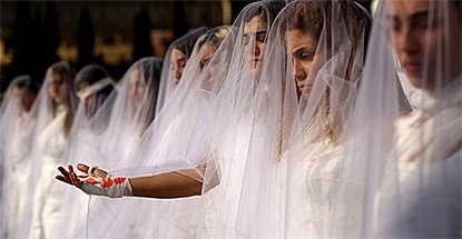 Nio libanesiska kvinnor klädda i vitt och med massor av slöjor står uppradade. En kvinna sträcker fram handen, som har ett blodigt bandage på sig.