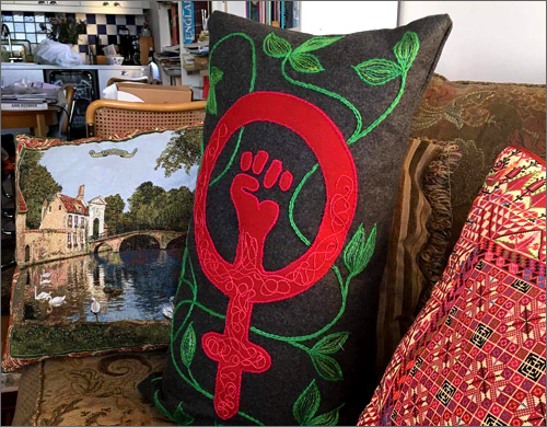 Kuddar i en soffa där den ena har ett kvinnomärke i rött tyg och broderi